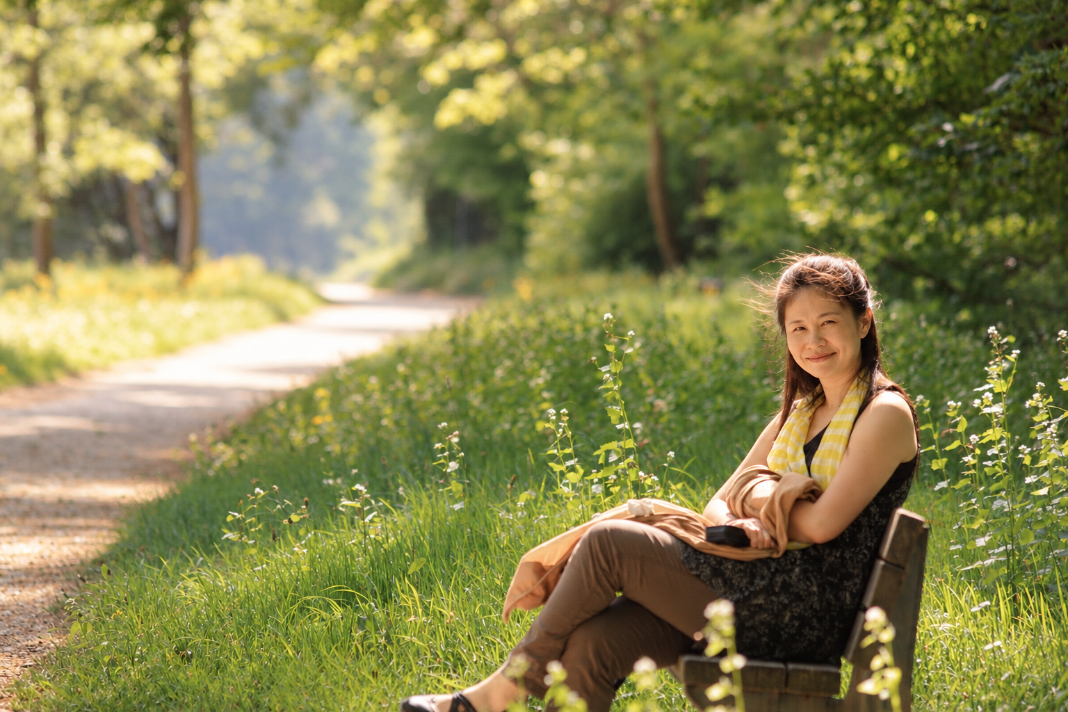 Dr. Liwen Li sitzt auf einer Bank an einem Waldweg und lächelt in die Kamera.